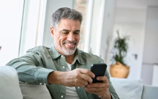Ein Kunde sitzt auf dem Sofa und liest erfreut eine Versandbestätigung auf seinem Smartphone