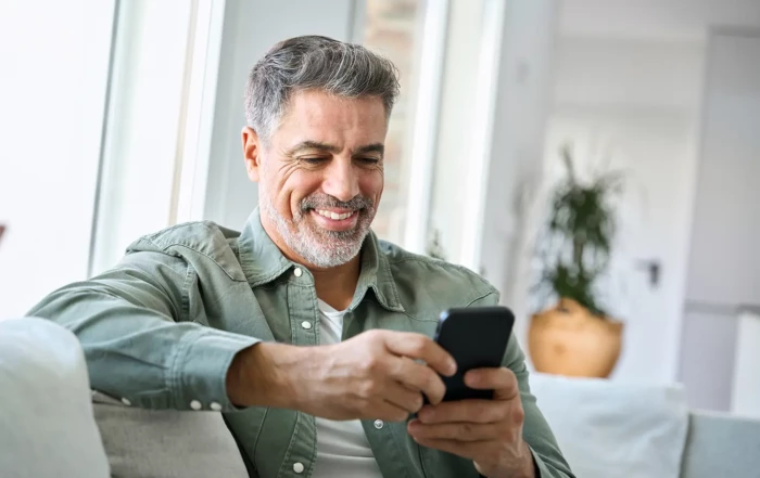 Ein Kunde sitzt auf dem Sofa und liest erfreut eine Versandbestätigung auf seinem Smartphone
