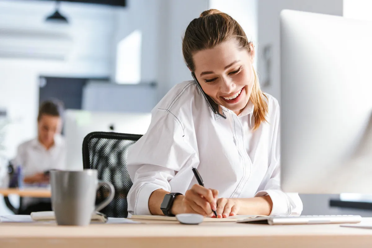 Die Top Funktionen für einen B2B-Online Shop - Frau sitzt telefonierend am PC und notiert sich Tipps mit einem Stift